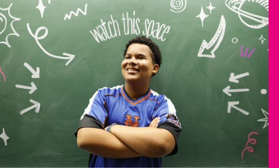 smiling youth in front of chalk board with the writing 'watch this space'